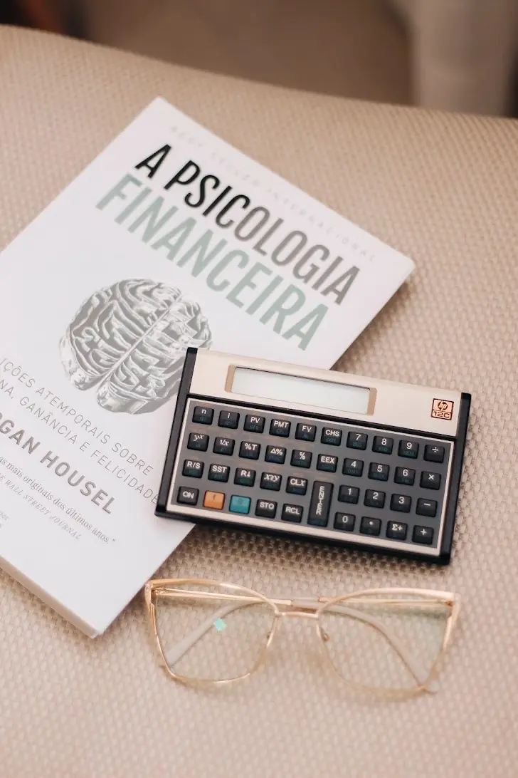 Livro de psicologia financeira, calculadora e óculos